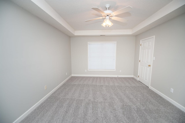 carpeted empty room featuring baseboards, a textured ceiling, a tray ceiling, and a ceiling fan