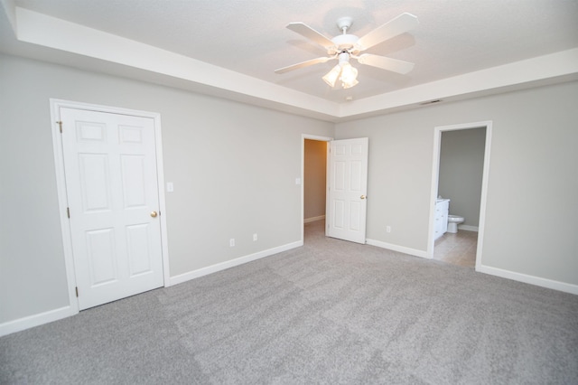 unfurnished bedroom with baseboards, connected bathroom, ceiling fan, carpet, and a tray ceiling