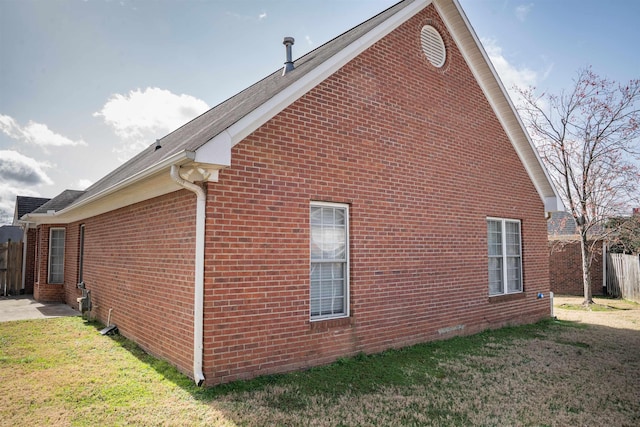 view of home's exterior featuring brick siding, a lawn, and fence