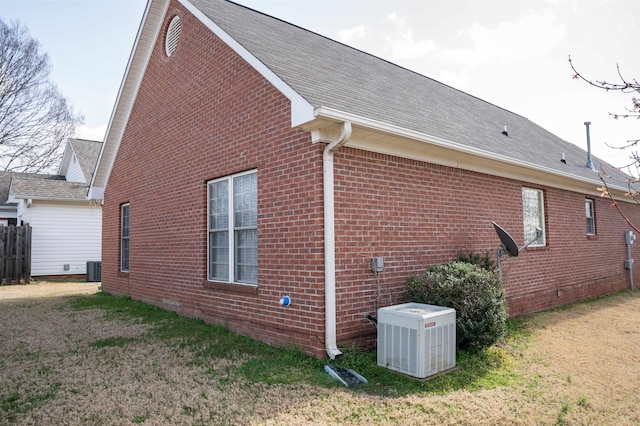 view of home's exterior featuring brick siding, roof with shingles, central AC unit, and a yard