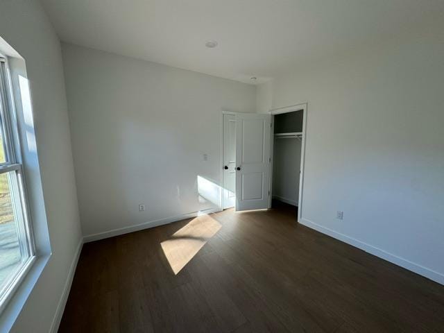 unfurnished bedroom with dark wood finished floors, baseboards, and a closet