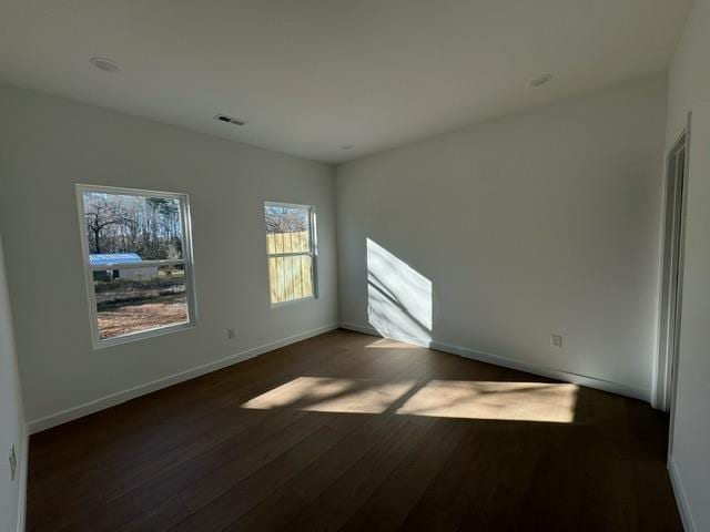 unfurnished room featuring visible vents, baseboards, and dark wood-style flooring