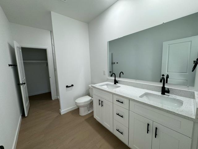 bathroom featuring double vanity, wood finished floors, toilet, and a sink