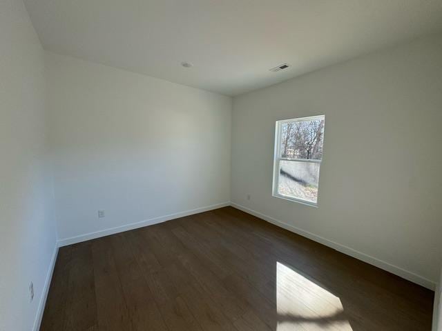 empty room with visible vents, baseboards, and dark wood finished floors