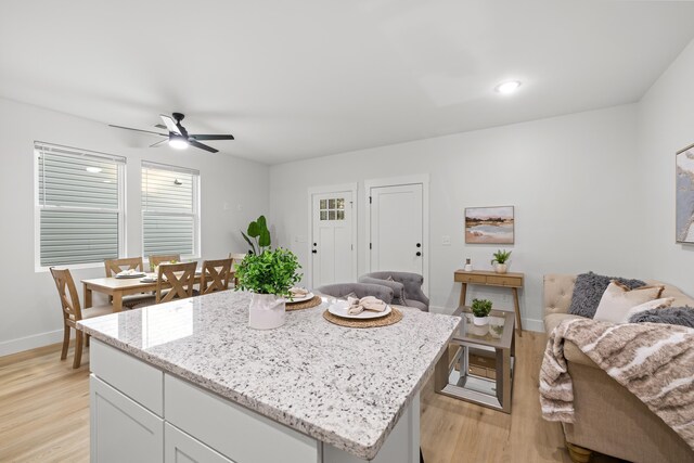 kitchen with light wood-type flooring, open floor plan, a center island, white cabinetry, and baseboards