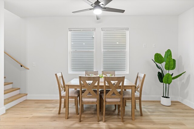 dining area featuring light wood finished floors, ceiling fan, stairs, and baseboards