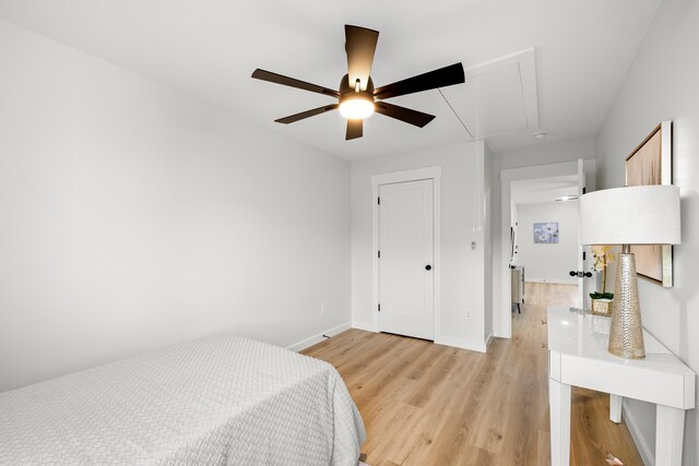 bedroom featuring attic access, light wood-style flooring, a ceiling fan, and baseboards