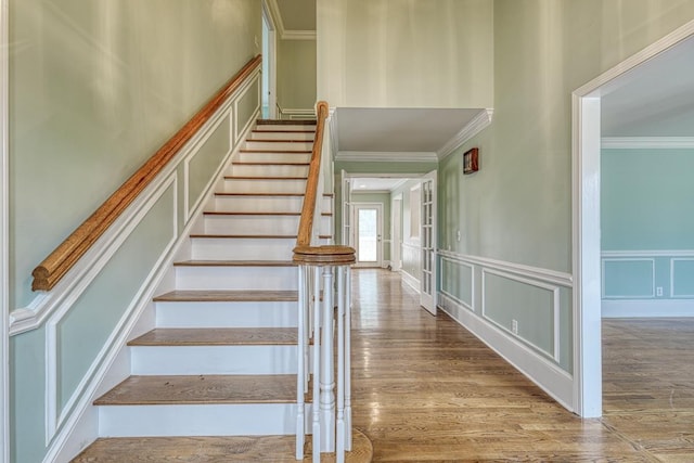 stairway featuring a decorative wall, crown molding, a wainscoted wall, and wood finished floors