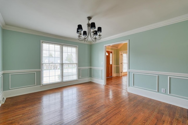 spare room with an inviting chandelier, wood finished floors, crown molding, and a decorative wall