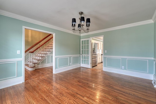 unfurnished room with wood finished floors, stairway, an inviting chandelier, crown molding, and a decorative wall