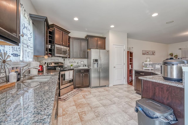 kitchen with a sink, stainless steel appliances, stone countertops, and dark brown cabinets