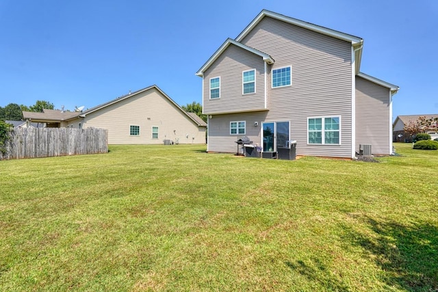 rear view of property featuring a lawn, central AC unit, and fence