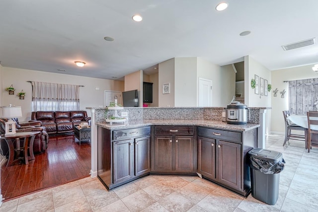 kitchen featuring light stone countertops, visible vents, recessed lighting, dark brown cabinets, and open floor plan