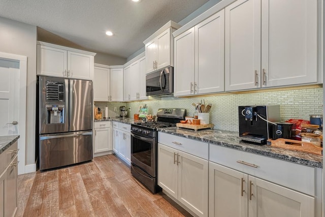 kitchen with dark stone counters, light wood-style flooring, decorative backsplash, white cabinets, and appliances with stainless steel finishes