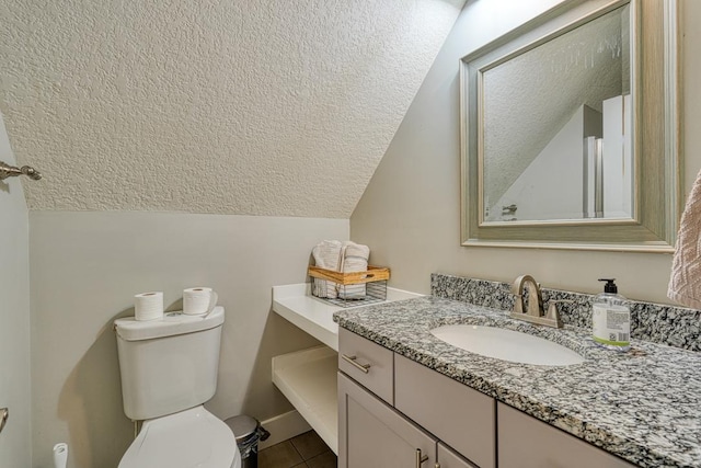 bathroom with toilet, vanity, vaulted ceiling, tile patterned floors, and a textured ceiling