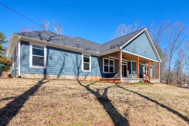 back of house with covered porch, a lawn, and a shingled roof