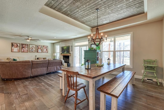 dining area with a raised ceiling, dark wood-type flooring, a fireplace, and a textured ceiling