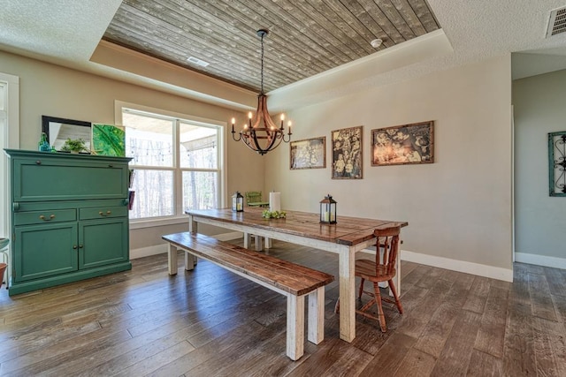 dining area with an inviting chandelier, baseboards, dark wood-type flooring, and a tray ceiling