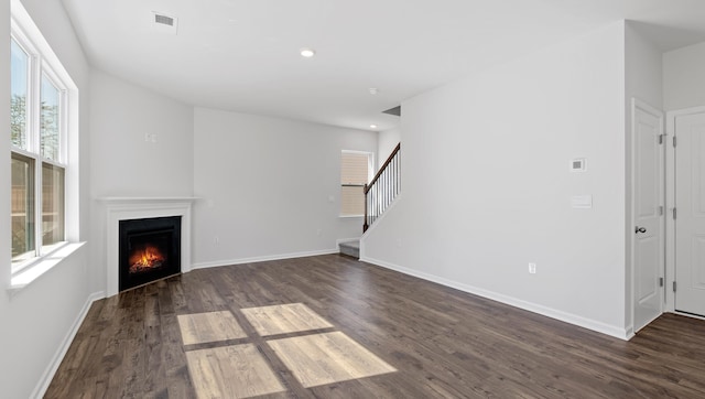 unfurnished living room with baseboards, a warm lit fireplace, dark wood-style flooring, and stairs