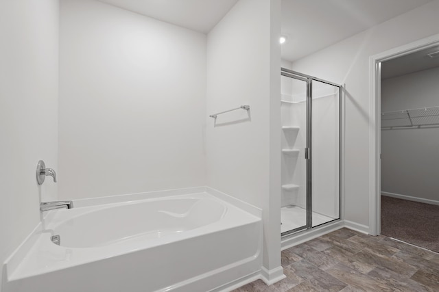 bathroom featuring baseboards, a spacious closet, a bath, and a shower stall