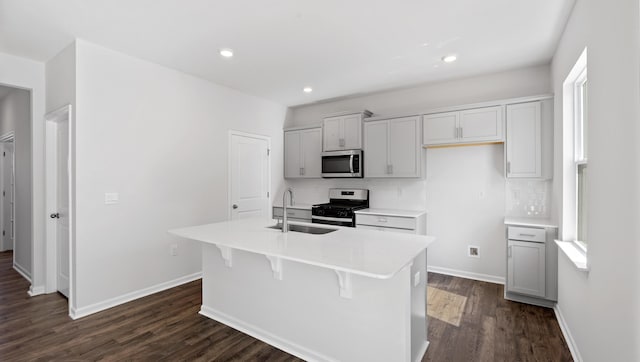 kitchen featuring an island with sink, a sink, stainless steel appliances, dark wood-type flooring, and tasteful backsplash