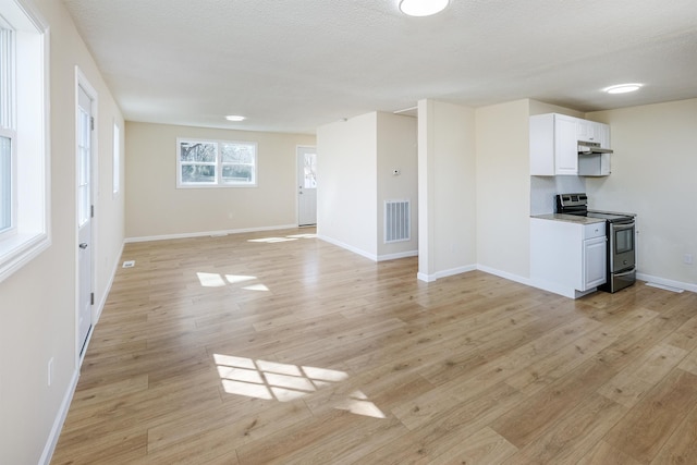 unfurnished living room with visible vents, baseboards, a textured ceiling, and light wood finished floors