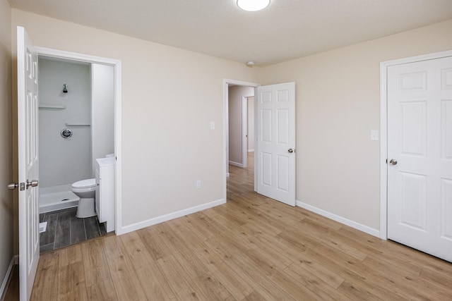 unfurnished bedroom with light wood-style flooring, connected bathroom, and baseboards