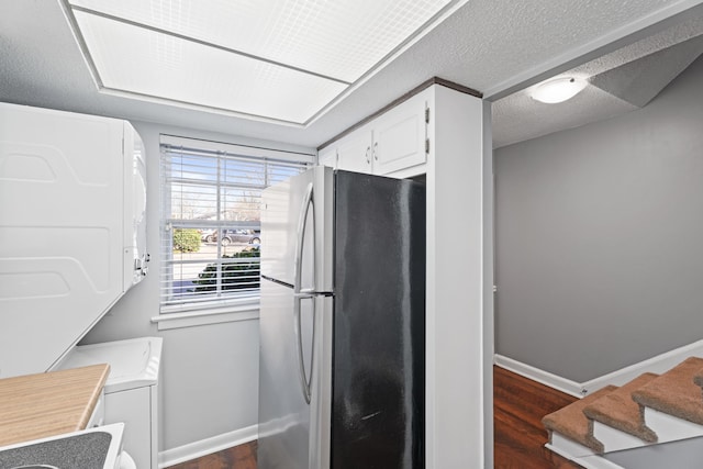 kitchen with white cabinetry, baseboards, stacked washer and dryer, freestanding refrigerator, and a textured ceiling