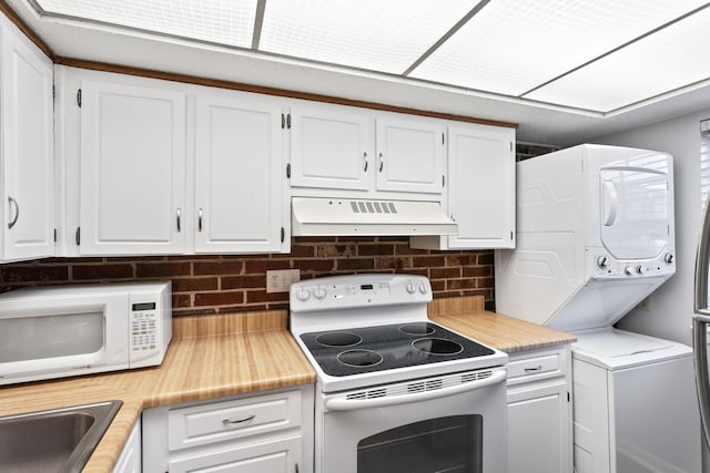 kitchen featuring under cabinet range hood, white appliances, white cabinetry, and stacked washing maching and dryer