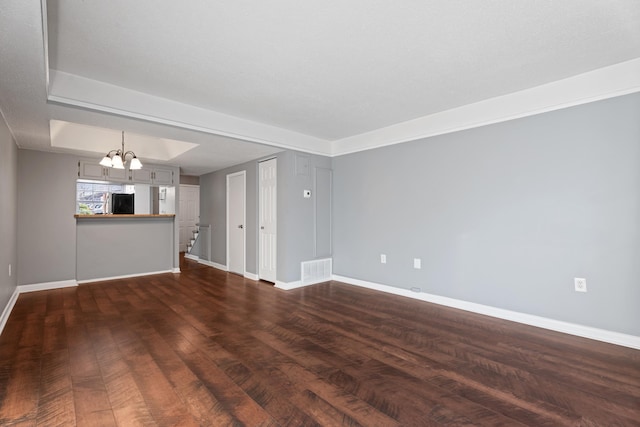 unfurnished living room with visible vents, a tray ceiling, dark wood finished floors, an inviting chandelier, and baseboards