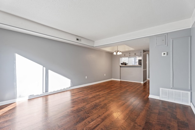 empty room with a notable chandelier, dark wood-style floors, visible vents, and baseboards