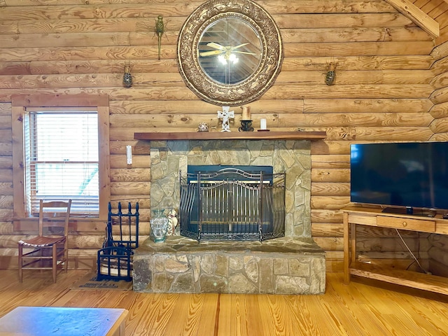 living room with rustic walls, a stone fireplace, and wood finished floors