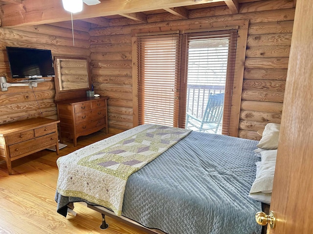 bedroom with log walls, beam ceiling, wood finished floors, and access to outside