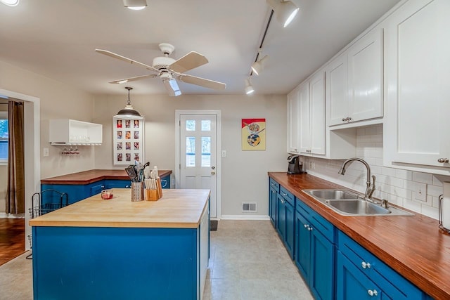 kitchen with blue cabinetry, a sink, butcher block countertops, white cabinetry, and backsplash