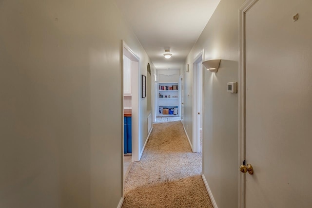 hall featuring light colored carpet and baseboards