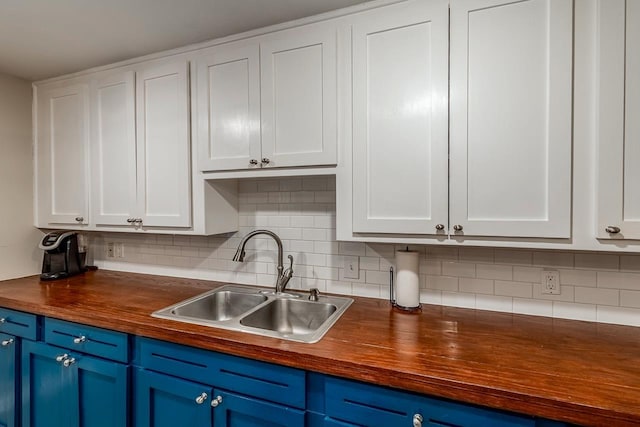 kitchen with butcher block countertops, blue cabinetry, white cabinets, and a sink