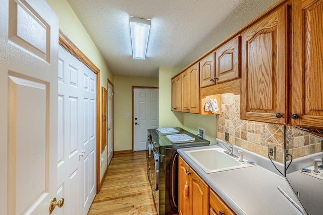 clothes washing area with washing machine and clothes dryer, cabinet space, a sink, light wood-style floors, and a textured ceiling