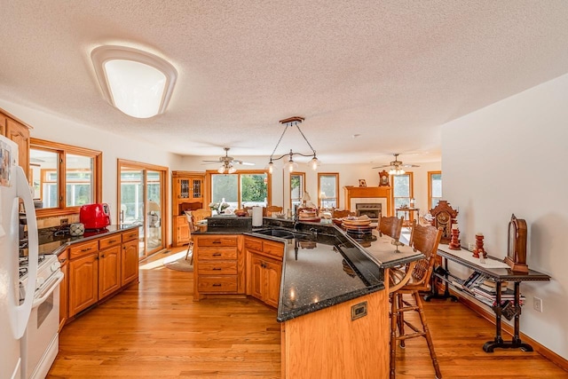 kitchen featuring a kitchen bar, light wood-type flooring, a sink, white appliances, and a fireplace