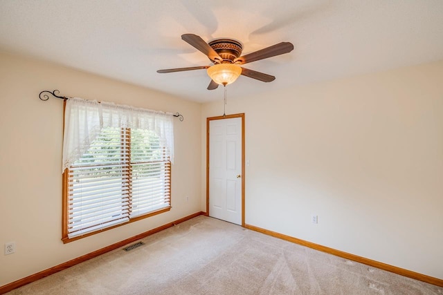 spare room featuring a ceiling fan, light colored carpet, visible vents, and baseboards