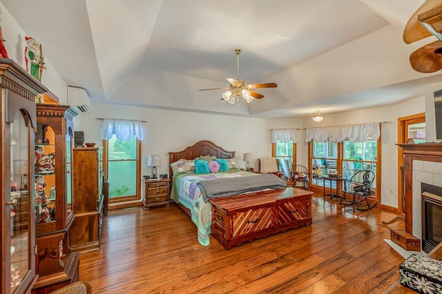 bedroom with a tray ceiling, an AC wall unit, a fireplace, and wood-type flooring