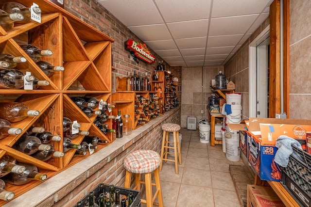 wine cellar featuring a paneled ceiling, brick wall, and tile patterned flooring