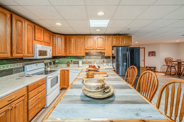 kitchen with decorative backsplash, white appliances, brown cabinetry, and light countertops