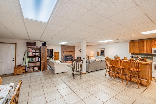 living area featuring a brick fireplace, light tile patterned flooring, and a drop ceiling