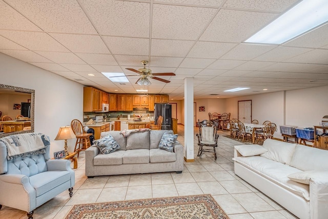 living room featuring a drop ceiling, light tile patterned flooring, and a ceiling fan