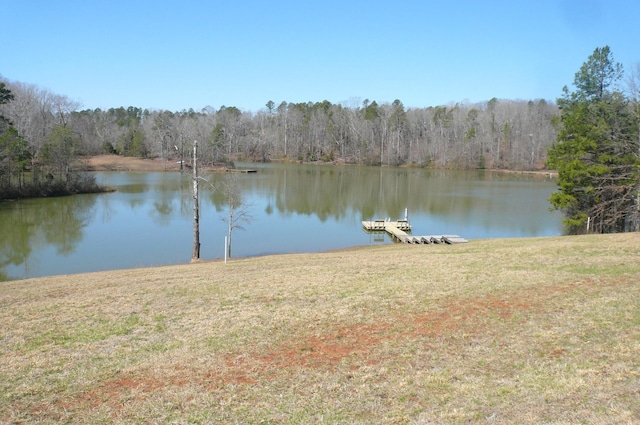 dock area featuring a lawn, a wooded view, and a water view