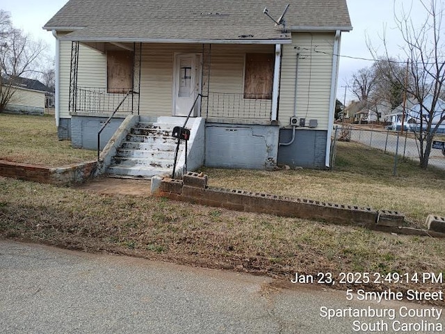 bungalow-style house with a front lawn, fence, covered porch, and roof with shingles