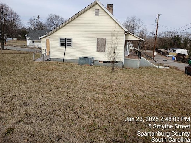 view of side of home with central air condition unit, a yard, covered porch, and a chimney