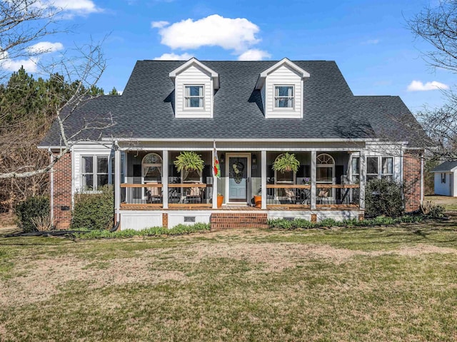 new england style home with brick siding, covered porch, a shingled roof, and a front lawn