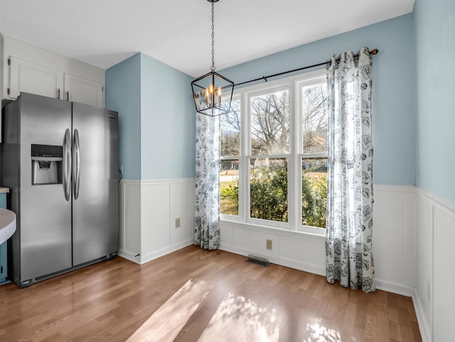 unfurnished dining area with wood finished floors, visible vents, a wainscoted wall, a textured ceiling, and a chandelier