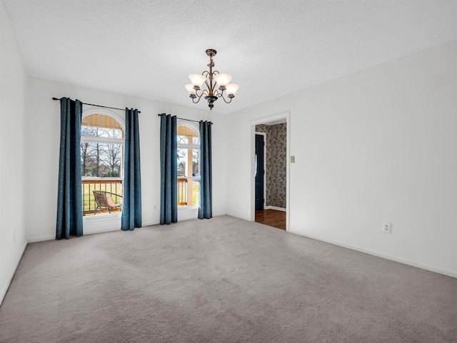 spare room with a textured ceiling, carpet flooring, and a chandelier